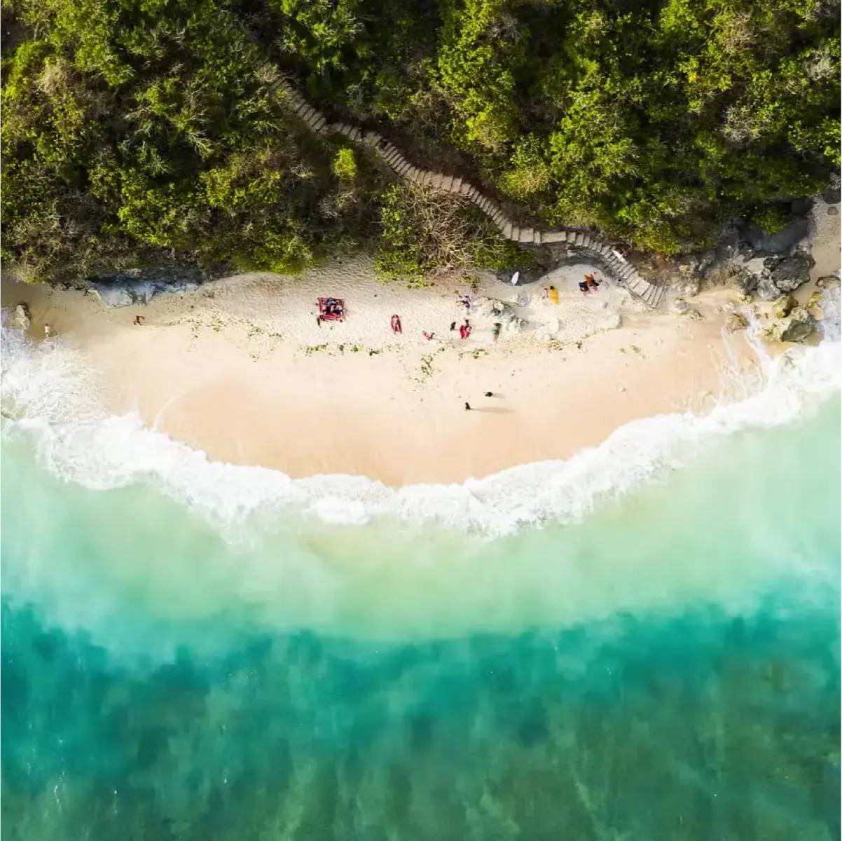 Aerial view of a pristine beach with turquoise water, soft waves, and lush green foliage in the background.